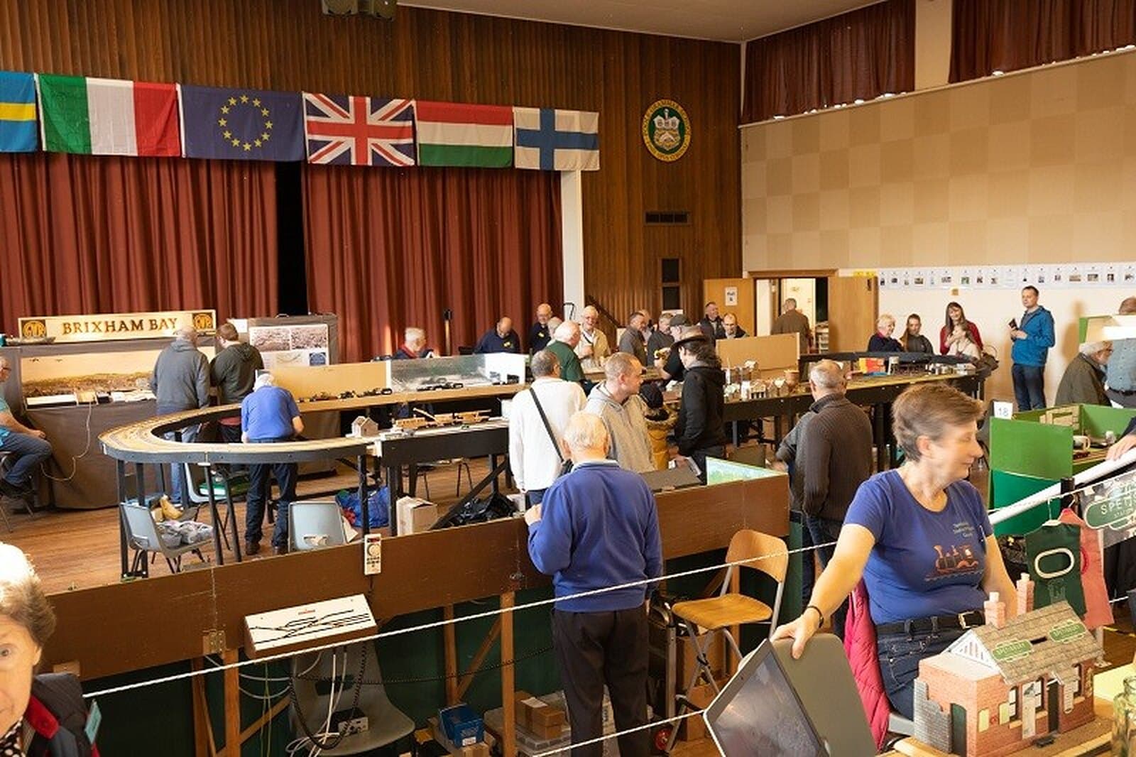 A busy exhibition hall in 2019, with layouts, visitors and flags overhead